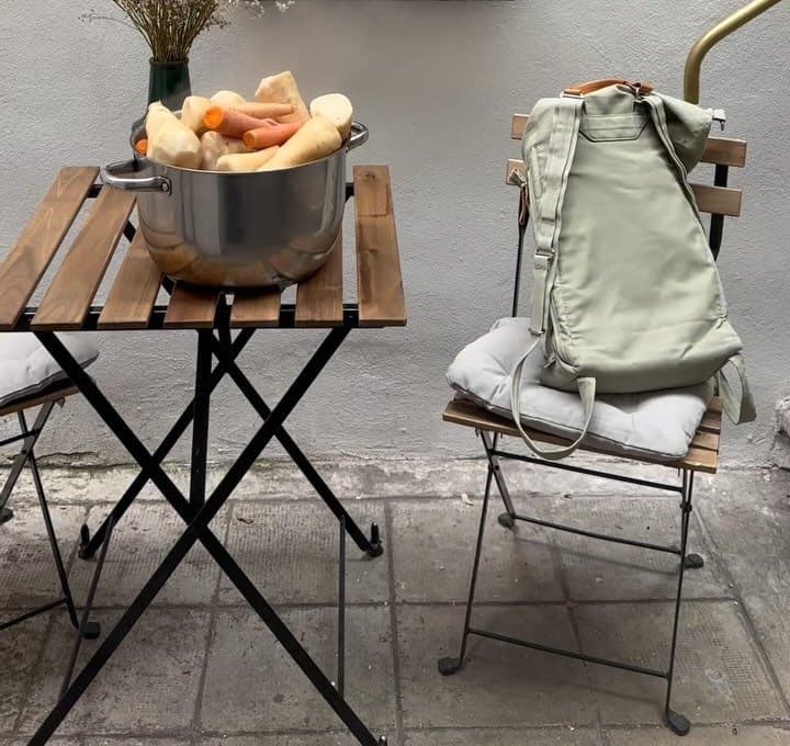 O masă pliantă cu o oală de legume și un buchet de flori uscate, lângă un scaun cu un rucsac